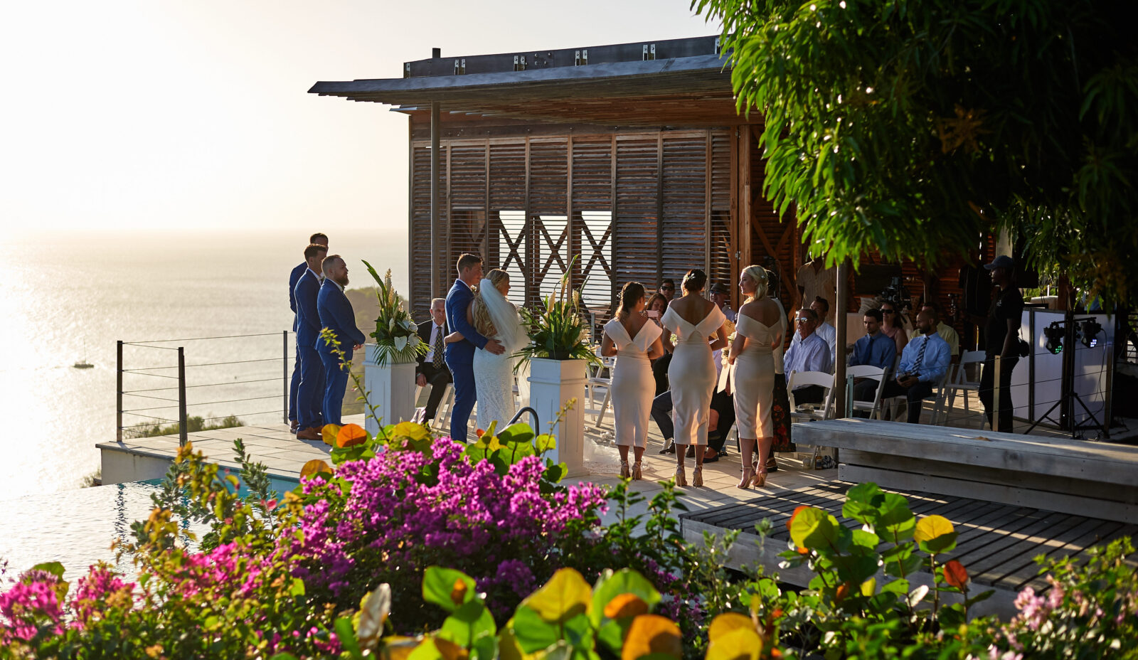 A small wedding ceremony on an outdoor terrace with the Caribbean sea in the background and pink and green garden flowers in the foreground
