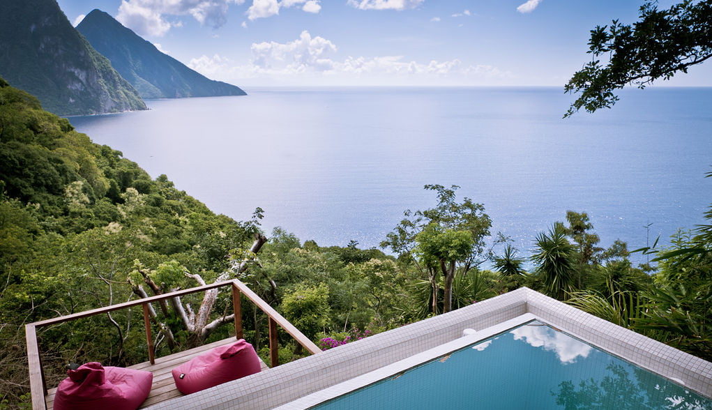 A corner of the blue plunge pool and adjacent sun deck with pink bean bags at the Lodge at Cosmos St Lucia, looking over the caribbean Sea and the Pitons