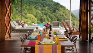 A celebratory dining table laid with colourful crockery and glasses at Cosmos St Lucia, with a view of the sun terrace and pool in the background
