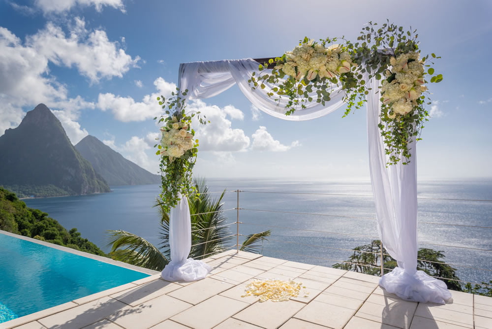 A floral arch stands on a sun terrace, with a view of the Pitons behind