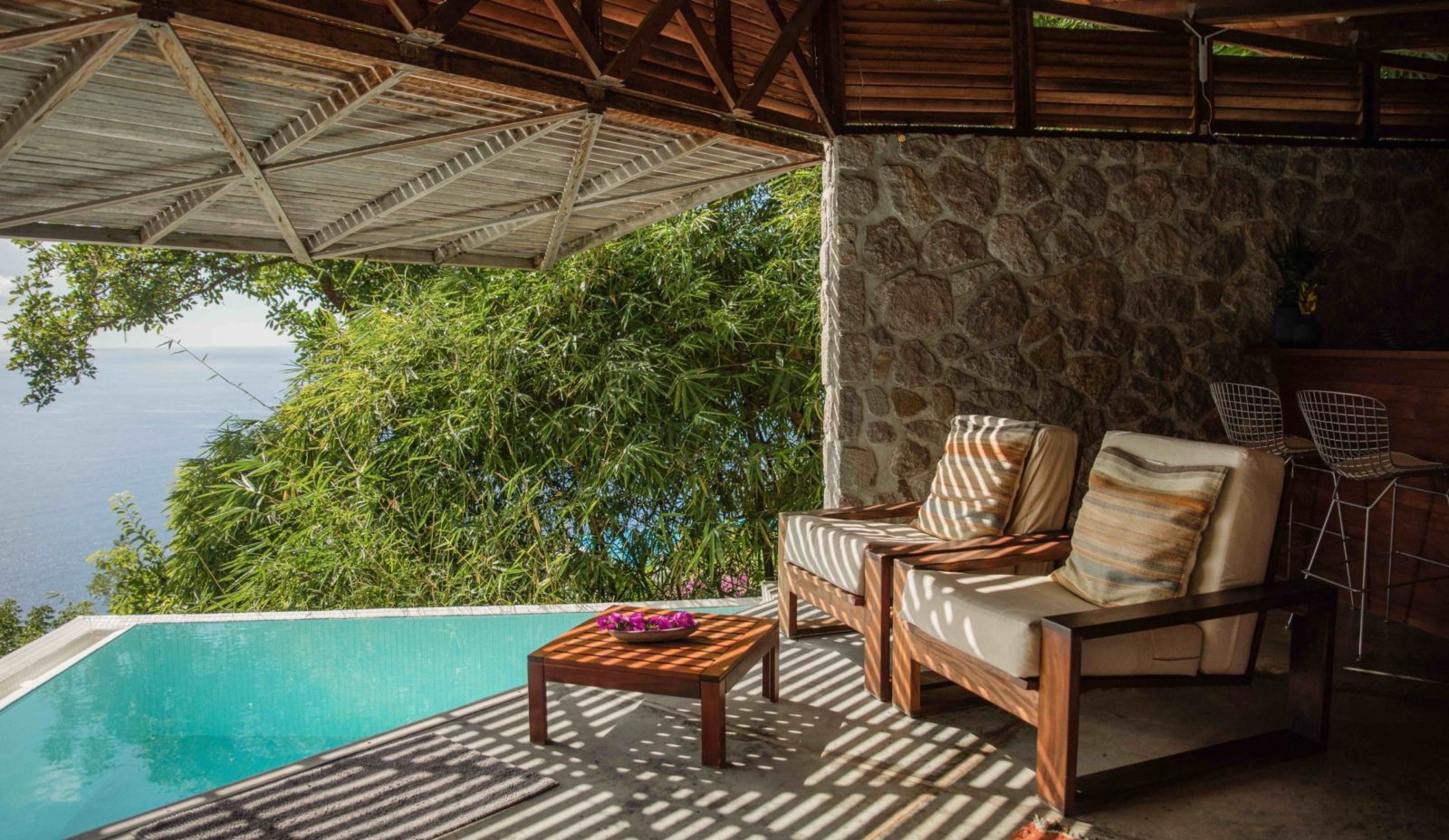 two armchairs have a table infront of them, looking onto the plunge pool and Caribbean Sea beyond