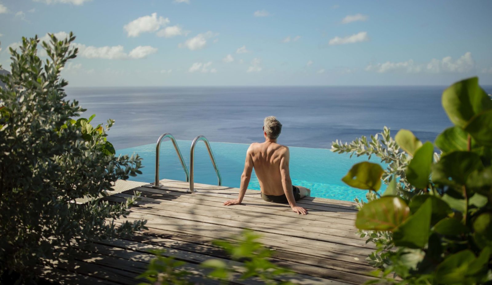 A man sits on the side of the infinity pool at Cosmos St Lucia, facing towards the Caribbean Sea