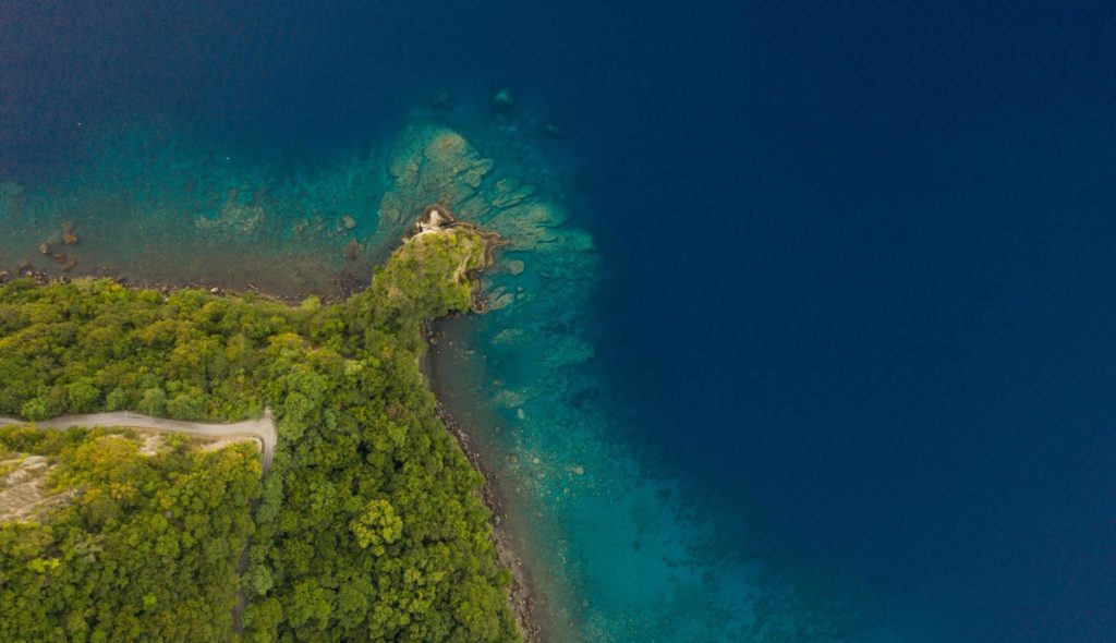 An aerial view of the coastline near Cosmos St Lucia showing a deep blue sea changing to turquoise along the shorline and green vegetation on the land