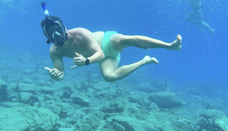 A man floats in clean blue water, wearing a snorkel as he floats above coral at Sugar Beach St Lucia.