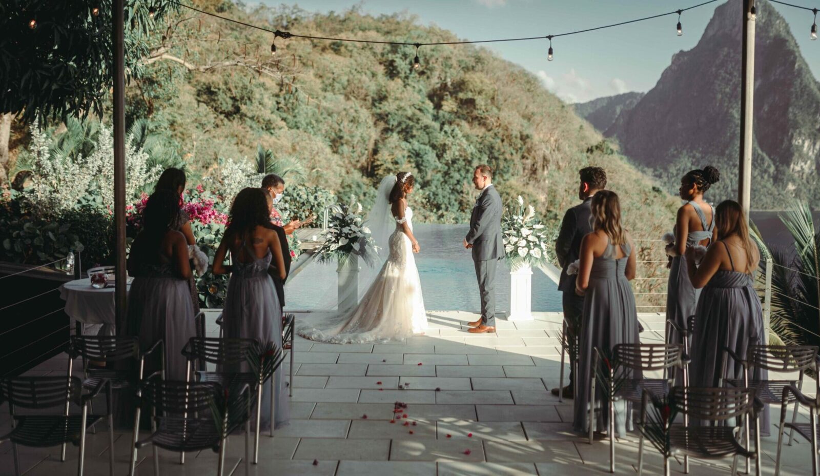 An interacial couple face each other as they say their wedding vows ona terrace infront of a small group of loved ones